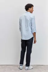 Camisa de corte regular, color celeste con rayas verticales blancas muy finas, cuello clásico y mangas largas con puños abotonados.