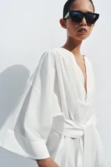 Vestido tipo túnica de corte evasé, color blanco, con escote en pico, mangas por debajo del codo y cinturón ajustable del mismo tejido.