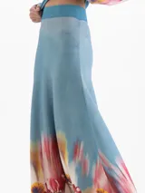 Pollera larga de tiro alto con calce evasé, confeccionada en tejido celeste con cintura elastizada lisa y estampado floral multicolor en el ruedo.