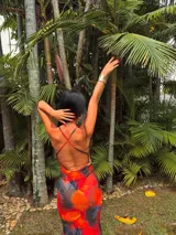 Vestido largo de microtul multicolor con estampado abstracto en tonos naranja, rojo, negro y azul. Presenta escote en V con ribete de encaje negro, breteles finos regulables y espalda descubierta.