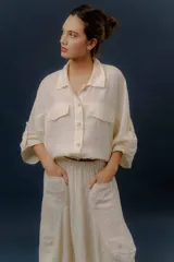Campera liviana de lino en color beige, con cuello camisero, cierre frontal de botones, mangas largas amplias y bolsillos con solapa en el pecho.
