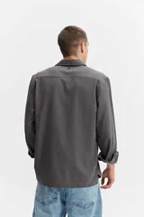 Camisa rústica de manga larga color gris oscuro, con cuello clásico, cierre frontal con botones y un bolsillo aplicado en el pecho.