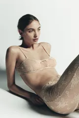 Pantalón tipo legging de encaje color dorado/beige, con patrón floral y acabado semitransparente. Presenta cintura y puños elásticos.