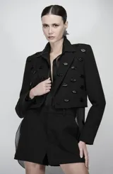 Blazer cropped negro de sastrería estructurada, con mangas largas, solapas clásicas y un diseño corto en la cintura. Está decorado en la parte frontal y las solapas con apliques tridimensionales en relieve con forma de labios de acabado esmaltado brillante.