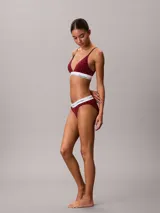 Bralette Calvin Klein de corte triangular, confeccionado en mezcla de algodón elástico y modal, con estampado gráfico en tonos rojos y banda elástica inferior en color blanco con el nombre de la marca en contraste.