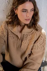 Sweater de punto color beige con cuello polo y detalles de tejido crochet en la parte superior y mangas. Presenta una textura acanalada en el cuerpo y un diseño romántico.