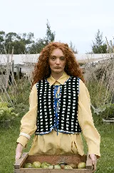 Chaleco tejido a mano en crochet con diseño de cuadros en azul y blanco, con bordes en color verde. Es una prenda reversible con cierre frontal mediante cordones ajustables.