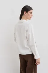 Remera de manga larga color blanco con cuello polo y cierre frontal parcial. Presenta costuras a la vista en contraste y un pequeño bordado en el pecho. El diseño incluye una abertura lateral en el ruedo.