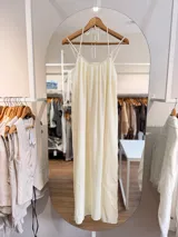 Vestido largo color marfil de silueta amplia y caída fluida, con escote fruncido, tiras finas para anudar al cuello y tirantes dobles. Cuenta con tajo en la espalda y forro corto interno.