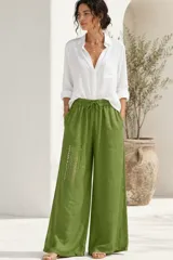 Pantalón palazo de lino verde militar, de corte holgado, con cintura elástica y cordón ajustable. Cuenta con bolsillos laterales y detalle de bordado decorativo en una pierna.