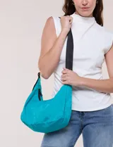 Cartera bandolera de lona naranja en forma de medialuna, con correa ajustable negra y cierre principal.