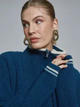 Sweater de tejido de punto grueso en color azul, con cuello alto y medio cierre frontal. Presenta detalles de rayas en contraste en los puños y el ruedo, con un diseño de corte holgado.