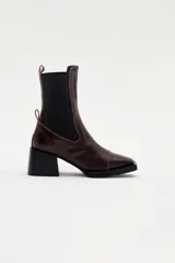 Bota tipo chelsea de cuero color bordó, con paneles laterales elásticos en color negro, taco cuadrado y suela con plataforma delantera.