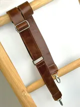 Correa ajustable para cartera confeccionada en cuero marrón con costuras a la vista y herrajes metálicos plateados.