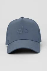 Gorra tipo trucker de alto rendimiento con corona estructurada, paneles traseros perforados para mayor ventilación y cierre ajustable con velcro. Presenta el logo de la marca bordado en el frente.