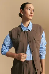 Chaleco negro de corte estructurado con cuello redondo, cierre frontal oculto y lazo ajustable en la cintura. Presenta dos bolsillos frontales con solapa y diseño de hombros caídos.