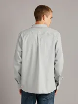 Camisa gris melange de manga larga con cuello clásico, cierre frontal con botones, bolsillo de parche en el pecho y corte recto.