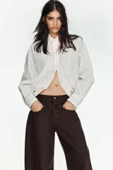 Camisa de corte oversize con estampado de rayas verticales, cuello solapa, cierre frontal con botones y mangas largas con puños abotonados.