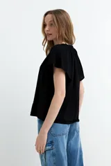 Blusa de manga corta color negro, con escote en V y frunces en los hombros, de diseño holgado y ligero.