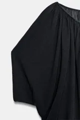 Top estilo túnica color negro confeccionado en punto fino, de manga corta y cuello redondo con frunces. Presenta un diseño holgado con abertura delantera en el bajo.