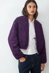 Campera bomber corta de pana color violeta, con cierre frontal de cremallera, cuello redondo y mangas largas con puños elásticos.