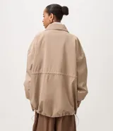 Campera cortaviento oversized color beige, de cuello alto, mangas largas con puños elásticos, bolsillos frontales con solapa y cordón ajustable en la cintura.