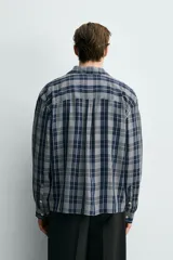 Camisa de corte relajado confeccionada en tejido fluido con mezcla de viscosa y acetato. Presenta un diseño a cuadros, cuello solapa, manga larga con puños abotonados, bolsillo plastrón en el pecho y cierre frontal con botones.