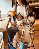 Bolso marrón de cuero gamuza con detalles de correa en cuero mostaza. Tiene una correa corta para llevar como bolso de mano y una correa larga extraíble y regulable. En el interior tiene bolsillo y llavero.