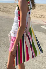 Bolsa de tejido canvas con estampado de rayas verticales en tonos rosado, verde, beige y rojo, con asa de hombro decorada con nudos.