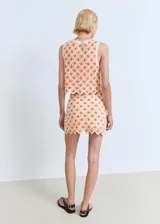 Minifalda de crochet color beige con estampado floral en tonos naranjas, corte recto y bajo festoneado.