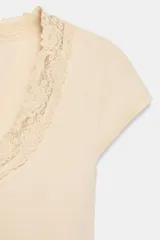 Top color beige claro, confeccionado en hilatura con mezcla de algodón. Presenta cuello redondo amplio con detalle de encaje combinado a tono y mangas muy cortas.