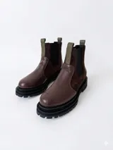 Bota tipo chelsea con plataforma dentada, confeccionada en cuero con combinación de texturas en tonos marrón y verde oliva. Presenta paneles laterales elásticos y tiradores en la parte superior.
