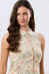 Camisa sin mangas de lino y algodón, con estampado floral en tonos violeta y verde sobre base beige, cuello camisero y cierre frontal de botones.