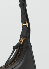 Riñonera de diseño minimalista en color negro, confeccionada en material efecto piel con acabado liso. Presenta una forma curva estructurada, cierre superior con cremallera y una correa ajustable con hebilla metálica que permite llevarla al hombro o cruzada.