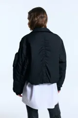 Campera tipo bomber de nylon con ligero relleno, corte cropped y ajuste recto. Presenta cuello camisero, cierre frontal metálico, puños de ribb y bolsillos frontales con tapa. Incluye un bolsillo decorativo con cierre en la manga y bordado a tono en el frente.