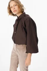 Camisa de corte holgado color marrón chocolate, con cuello clásico, cierre frontal de botones y mangas largas abullonadas con frunces en los hombros.