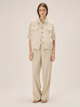 Chaquetas de lino bicolor en tonos blanco y beige, con diseño holgado, cuello alto, cierre frontal de botones, bolsillos con solapa en el pecho y mangas cortas con presilla y botón.