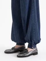 Jeans de mezclilla azul oscuro, modelo balloon con tiro alto, pierna muy ancha y puños ajustables con botón en el tobillo para crear volumen.