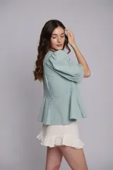 Chaqueta o blusa de tejido natural color verde menta, con mangas balloon y un botón decorativo en forma de estrella de mar. El cuerpo tiene un ruedo evasé.