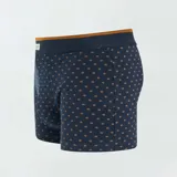 Pack de tres boxers de algodón elástico, uno liso color ocre, uno a rayas horizontales azul y ocre, y uno azul con estampado de hojas color ocre.