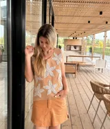Chaleco de cuero tostado en el frente con apliques de grandes flores de crochet blancas, y espalda de tejido de punto de algodón. Presenta cuello redondo y diseño sin mangas.