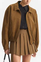 Chaqueta estilo bomber de color marrón, confeccionada en una mezcla de algodón y poliéster. Presenta cuello tipo camisa, cierre frontal y elástico en el bajo.