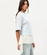 Remera overboxy de algodón color celeste, con cuello redondo, mangas cortas amplias y bajo asimétrico con aplicación de encaje blanco.