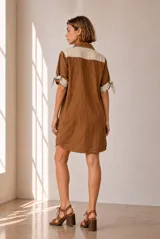Vestido corto de lino color beige, de corte recto y holgado, con cuello polo y cierre frontal parcial con botones. Las mangas cortas cuentan con detalles de tiras para anudar en los puños.