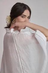 Camisa blanca de lino con cuello clásico, cierre frontal con botones, mangas anchas 3/4 y detalles de bordado calado en el canesú y los puños.