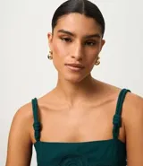 Blusa verde oscuro de viscolino con tirantes dobles ajustables mediante nudos. Presenta un corpiño estructurado con un detalle de flor en relieve en la parte delantera y smock en la espalda para un mejor ajuste. La prenda tiene un bajo peplum.