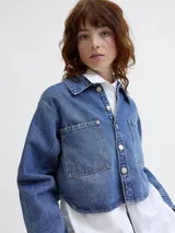 Sobrecamisa cropped de denim azul medio, con cuello clásico, mangas largas globo y dos bolsillos de parche con tapa en el pecho.
