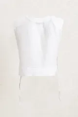 Remera crop top de lino color blanco, con cuello redondo y hombreras marcadas que le dan una estructura definida. Presenta un corte recto y holgado con aberturas laterales ajustables mediante cordones.