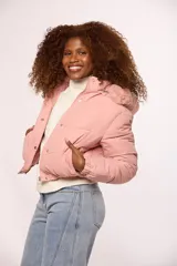 Campera bomber de nylon color rosado, con diseño acolchado, cierre frontal con cremallera y botones a presión, y capucha con borde de piel sintética al tono.