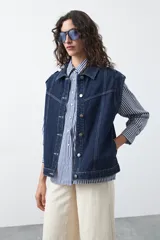 Chaleco de jean en tono celeste claro, con corte recto, cuello camisero, cierre frontal con botones metálicos y costuras visibles.